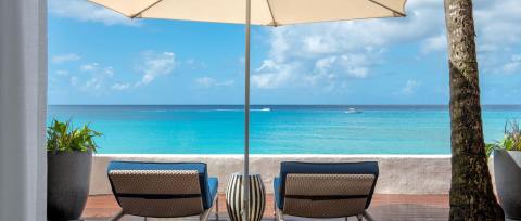 The image shows a serene beachfront view from a shaded outdoor terrace