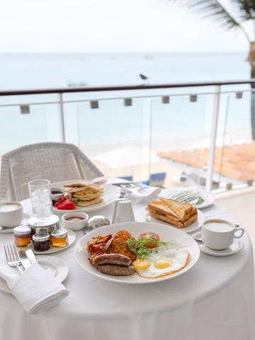 This image features a breakfast set up on a table overlooking a scenic beach