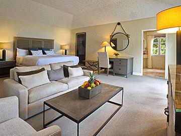 This image shows a neatly appointed hotel or possibly a residential room that features a living area and a bedroom partitioned by a partial wall