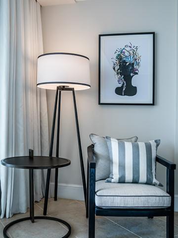 In the image, there is a cozy corner of a room that includes a black frame chair with gray upholstery and a white-and-gray striped cushion