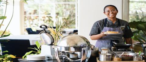 This image features a cheerful woman working in a bright and welcoming buffet or live cooking station within a restaurant
