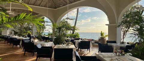 The image shows a beautifully set open-air dining area with a tropical aesthetic, likely part of a luxury resort or restaurant