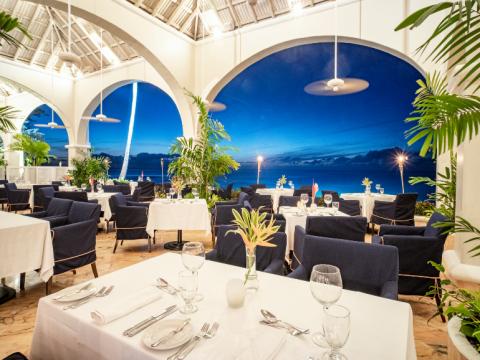 This image shows an elegant restaurant interior with a stunning view of the ocean at night