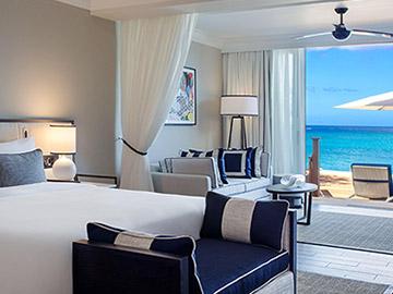 The image depicts a luxurious bedroom leading out to a terrace with a stunning ocean view