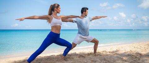 This image features a man and a woman practicing yoga on a sandy beach