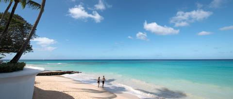 This image features a serene beach scene with clear turquoise waters and a bright blue sky scattered with clouds