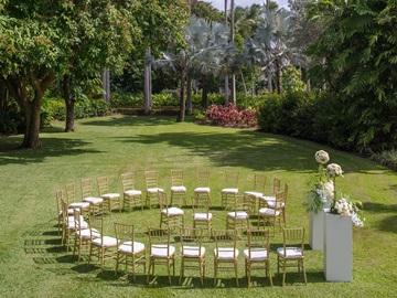 This image shows an outdoor venue set up for a ceremony, likely a wedding, given the chairs arranged in a semi-circle and a floral arrangement at the front
