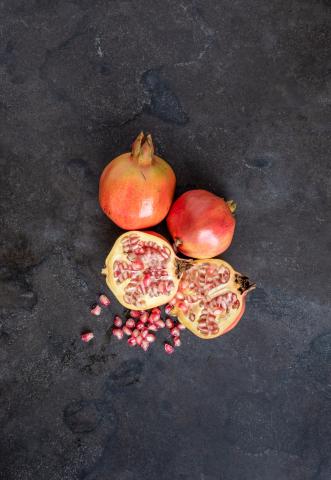 The image shows several pomegranates on a dark textured background