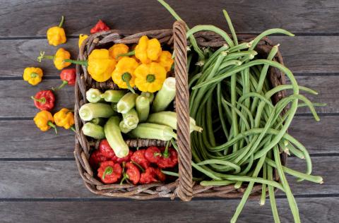 This image displays a variety of fresh vegetables arranged in a woven basket on a wooden surface