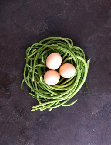 This image features a nest-like arrangement of green beans with three eggs nestled in the center
