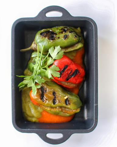 This image features a variety of grilled or roasted bell peppers in different colors (green, red, and yellow) placed in a black baking dish