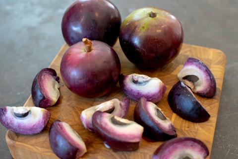 This image shows several whole and sliced star apples (also known as caimito) on a wooden cutting board