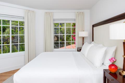 This image features a neatly arranged, well-lit bedroom with a large bed covered in white bedding