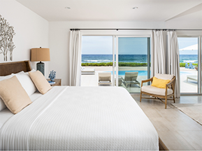 This image shows a modern and beautifully arranged bedroom with a view of the ocean through large glass windows