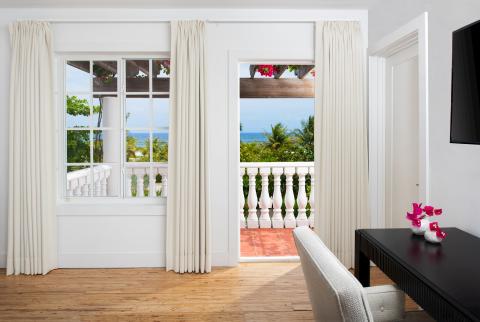 This image shows a stylish interior space leading onto a balcony with a scenic tropical view