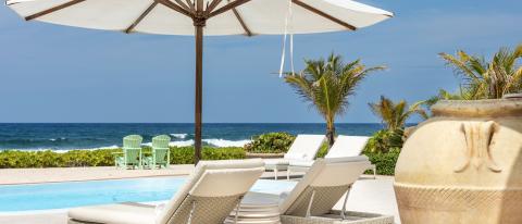 The image depicts a luxurious beachfront setting with a swimming pool