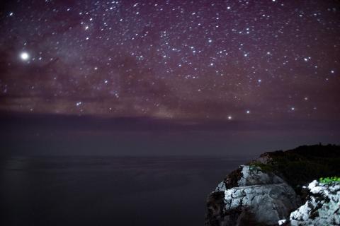 This image captures a stunning night sky filled with stars over a landscape which appears to include an ocean or a large body of water and cliff edges