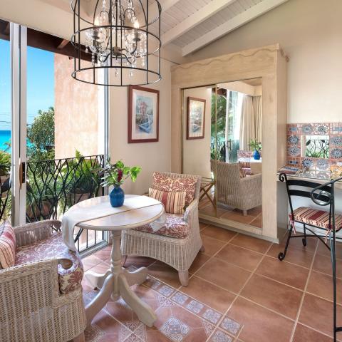 This image shows a cozy, well-decorated interior space opening to a balcony overlooking a scenic view, likely a body of water given the glimpse of blue through the railing