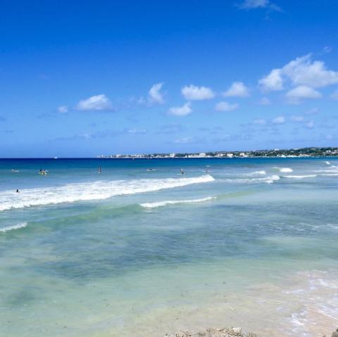 This image shows a beautiful sunny beach scene with clear turquoise waters and gentle waves
