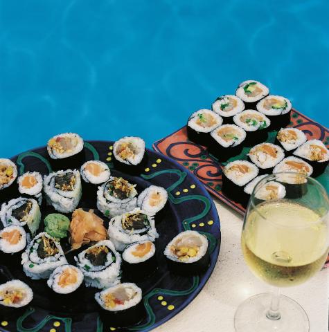The image displays a delightful arrangement of sushi on two decorative plates, one with a floral pattern and another with a circular geometric pattern, placed beside a swimming pool with the water providing a turquoise blue background