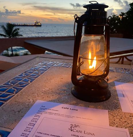 This image captures a serene dining scene at dusk, featuring a lit lantern on a table with Café Luna menus