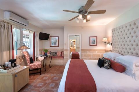 This image shows a well-appointed hotel room featuring a large bed with a plush, tufted headboard and various pillows