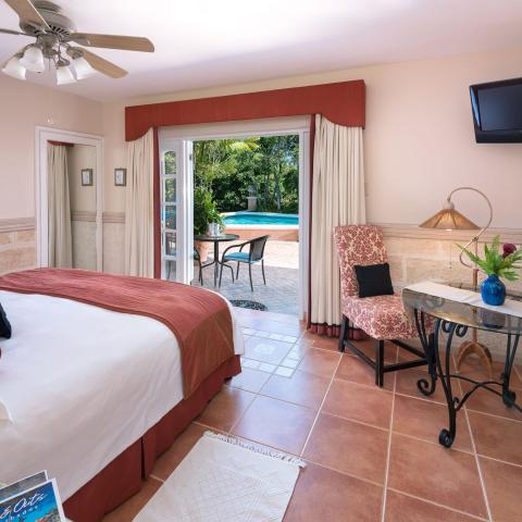 The image shows a well-appointed hotel room that opens to a private patio with a pool view