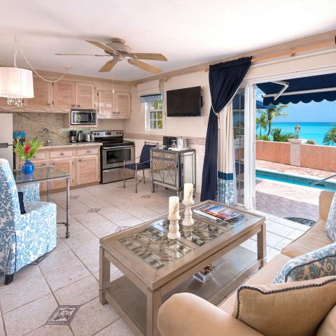 The image shows a beautiful interior that combines a living area and a kitchen, with an excellent view of a swimming pool area and a beach beyond