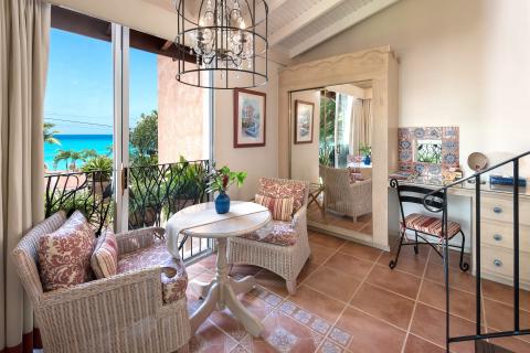 This image showcases a beautifully decorated, bright indoor space that leads to a balcony with a scenic view of the ocean and palm trees