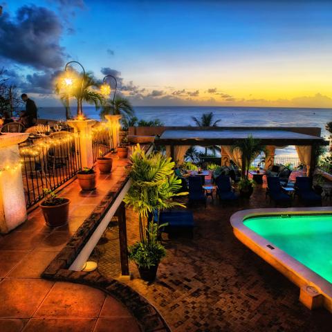 This image shows a beautifully lit outdoor terrace at dusk, overlooking the sea
