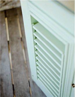 The image shows a close-up view of a pale green louvered door or panel, which appears to be part of a piece of furniture or perhaps part of a home