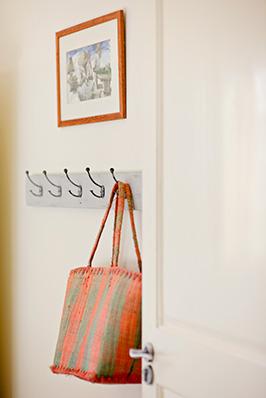 The image shows a home interior detail with a colorful bag hanging on a row of hooks on a white wall