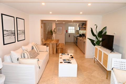 The image shows a modern, well-lit open-plan living space combining a living room and kitchen area