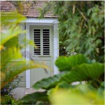 The image shows a small structure, possibly a garden shed or a quaint outdoor cottage, which is partially obscured by lush green foliage