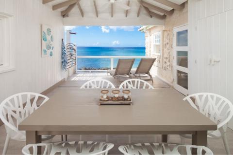 This image shows a beachfront patio setting with a beautiful view of a clear blue sea