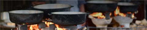 This image features multiple large pots placed on open fires