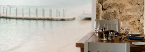 The image shows a dining setup on a wooden table located near a beach