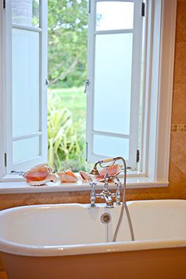 The image shows a bathroom setup, featuring a classic clawfoot tub near a window that looks out onto a green garden