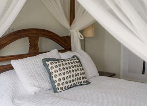The image shows a neatly made bed with a white bedspread and a decorative pillow