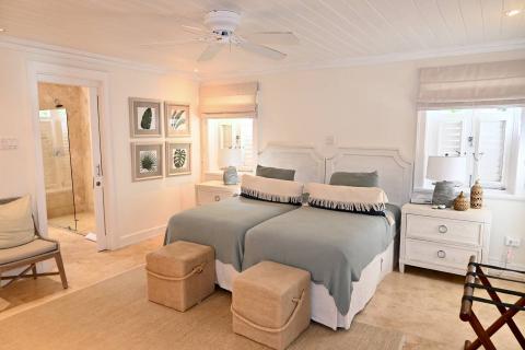 The image shows a stylishly decorated bedroom featuring two twin beds with muted teal bedspreads and decorative fringe-trimmed throw pillows
