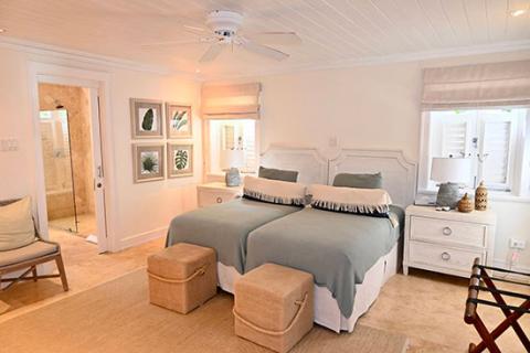 The image shows a well-appointed, bright bedroom featuring two twin beds covered with blue-gray bedding and white headboards