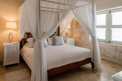 This image shows an elegantly styled bedroom featuring a large bed draped with a white, sheer canopy