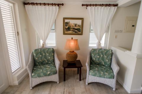 The image shows a cozy corner of a room featuring two wicker armchairs with green leaf-patterned cushions
