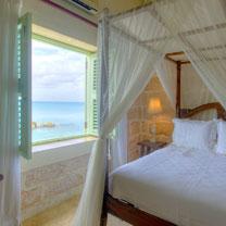The image shows a bedroom with a scenic view of the ocean through an open window