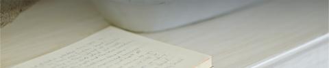 The image features an open notebook with handwritten text, lying on a wooden surface