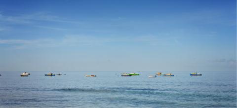 This image shows a tranquil seascape featuring a variety of boats floating on a calm body of water