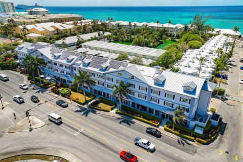 The image shows an aerial view of a coastal area, featuring multi-story buildings with blue and white exteriors and equipped with solar panels