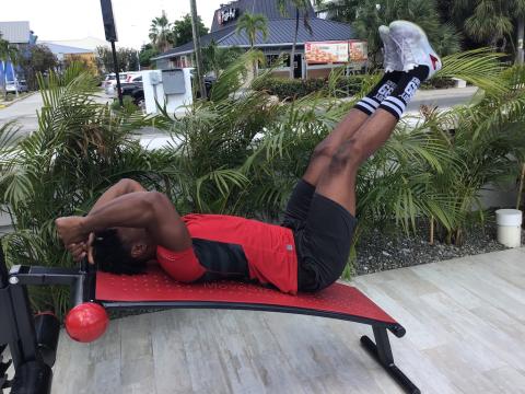In this image, a man is seen working out outdoors on a red and black exercise bench