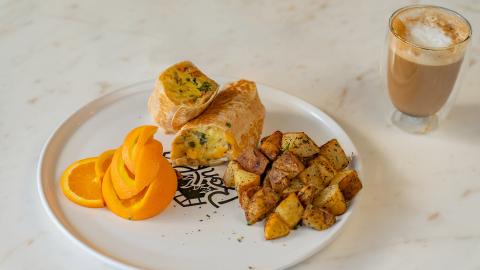 The image features a breakfast meal served on a white plate with a decorative logo at the center