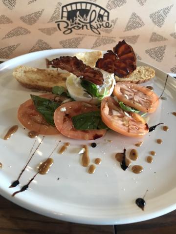 This image features a dish that includes slices of fresh tomatoes and mozzarella cheese garnished with basil leaves, presented on a white plate
